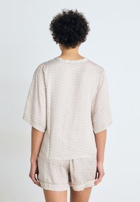 Ljust beige tvådelat pyjamas-set som består av en kortärmad topp och shorts. Tyget har ett subtilt geometriskt mönster och en mjuk textur.