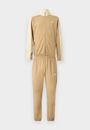 Φόρμα καμηλό από απαλό ύφασμα. Μπουφάν με ολόκληρο φερμουάρ, ψηλό γιακά, μανίκια σε εκρού χρώμα. Παντελόνι με ελαστική μέση και λεπτομέρεια με λογότυπο.