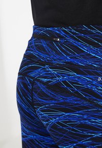 I leggings a vita alta presentano un motivo a onde geometriche blu su sfondo nero, con una piccola tasca con zip e cuciture testurizzate.