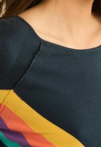 Pull en tricot marine avec un col large et des rayures diagonales orange, jaune, vert et violet sur le corps. Texture lisse.