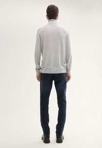 Maglione grigio chiaro con colletto alto, abbinato a jeans blu scuro. Il maglione ha maniche lunghe e una texture morbida. Scarpe nere completano l'outfit.