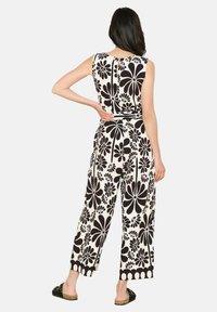 Bela in črna cvetlična kombinezon brez rokavov s širokimi hlačnicami, teksturiranega materiala in detajlom vezanja na hrbtu. Ima poudarjen rob v obliki valov.