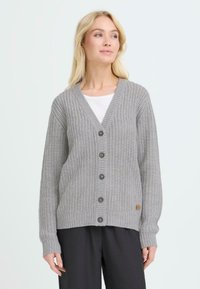 Cardigan de punto gris con escote en V, botones en la parte delantera, puños y dobladillo acanalados, y un pequeño parche de logo en el lado inferior.