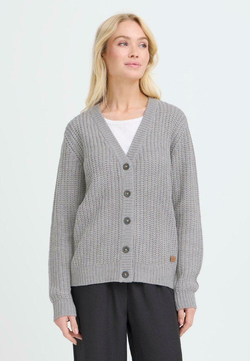 Cardigan de punto gris con escote en V, botones en la parte delantera, puños y dobladillo acanalados, y un pequeño parche de logo en el lado inferior.