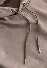 Tissu de sweat à capuche marron avec deux cordons passés dans des œillets métalliques, chacun se terminant par des embouts métalliques argentés.