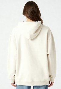 Felpa con cappuccio crema caratterizzata da una vestibilità ampia, polsini e orlo a costine, e una texture morbida, cuciture visibili, con un design semplice.