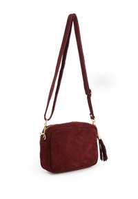 Bordeaux ruskind crossbody taske med lynlås, guld hardware, flad form og en frynseaccent på siden. Justerbar rem.