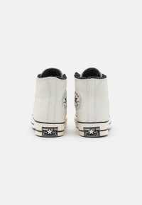 Vita läder hög-top sneakers med svart textilfoder, gummisula, klassisk märkespatch och svarta och vita randiga accenter.