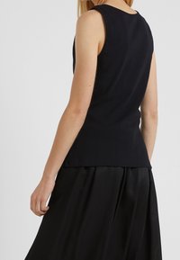 Top negro sin mangas con un diseño ajustado, fabricado en material de punto. Presenta un escote redondo y una textura suave, combinado con una falda negra fluida.
