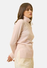 Vaaleanpunainen pooloneule, joka on valmistettu pehmeästä kankaasta. Neuleessa on ribbireunat hihoissa ja sivuissa, jotka lisäävät liikkuvuutta. Tasainen pinta koko neuleen ajan.