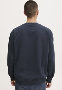 Sudadera azul marino con mangas largas, puños y dobladillo acanalados, y un pequeño detalle de parche en la parte posterior cerca del escote.