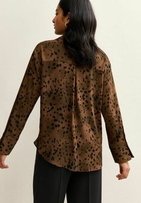 Camisa marrón de manga larga con un patrón de manchas negras, con una textura suave, dobladillo redondeado y costura en el yugo trasero.