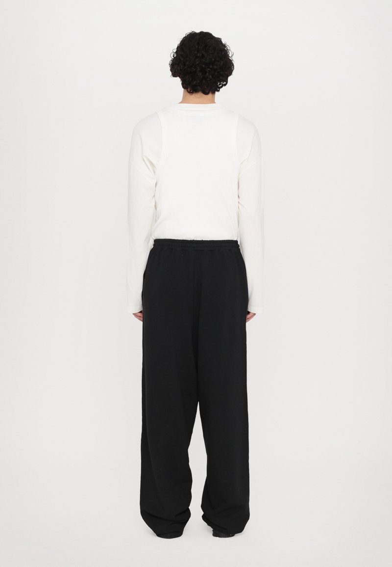 Weißes Langarmhemd und locker sitzende schwarze Hose, beide aus weichem Stoff. Das Hemd hat einen lässigen Schnitt; die Hose hat einen elastischen Bund.