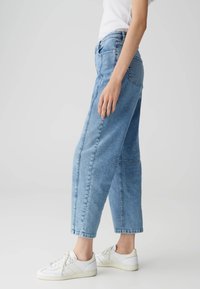 Jeans in denim azzurro chiaro con vestibilità comoda, caratterizzati da cuciture laterali, vita a metà altezza e risvolti, abbinati a sneakers bianche.