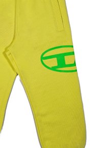 Pantaloni del gioco gialli realizzati in tessuto morbido, con un grande logo verde sulla gamba inferiore e tasche laterali. Design semplice e a gamba dritta.