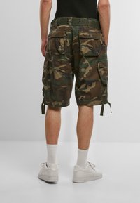 Cargo-Shorts im Camouflage-Print, aus Baumwolle. Verfügen über mehrere Taschen, einen entspannten Schnitt und verstellbare Seitengurte. Kombiniert mit weißen Sneakers.