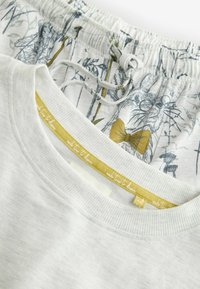 Camisa de algodón gris claro con un escote acanalado, superpuesta sobre pantalones de pijama estampados con conejitos de dibujos animados y vegetación en colores suaves.