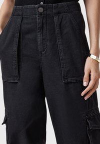 Zwarte denim cargobroek met een hoge tailleband, geplooide voorkant, zijzakken en zichtbare stiksels. Gladde textuur met een duurzaam materiaal.