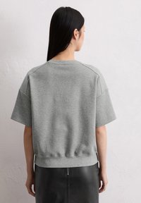 Gray cropped sweatshirt with short sleeves, ribbed neckline and hem, featuring soft texture and relaxed fit. Worn with a black skirt.