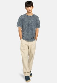 Vervaagde blauwe denim t-shirt met een ronde hals, gecombineerd met losse beige cargobroeken. Model draagt marineblauwe laarzen met een gestructureerde zool.