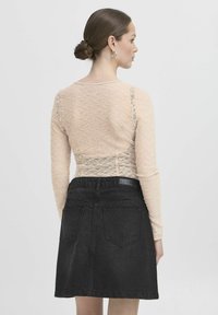 Top in pizzo a maniche lunghe color beige chiaro abbinato a una gonna di jeans nera. Il top presenta motivi floreali; la gonna ha un taglio classico e tasche.