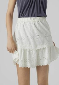 Vit bomullskjol med broderad ögla, volangkant och taklagskanter; har en elastisk midja för justerbar passform.