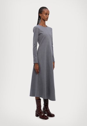 Gray long-sleeve dress with a round neckline, flowing A-line shape, made from a soft fabric. Paired with shiny burgundy knee-high boots.