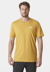 Camiseta de algodón amarilla con cuello redondo y mangas cortas, que presenta un logo blanco en el lado izquierdo del pecho. Diseño simple, sin patrones.