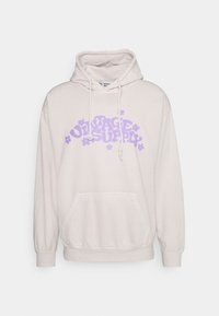 Beige hoodie med en ficka fram, dragsko-huva och lila "VINTAGE SUPPLY" text med blomsteraccenter. Mjuk, avslappnad tyg med ribbade ärmslut.