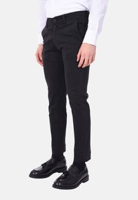 Chinos neri in cotone con un design aderente, gambe affusolate, tasche laterali e chiusura con un bottone. Indossati con mocassini neri lucidi.