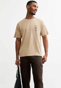 Camiseta de algodón beige de manga corta con gráficos florales abstractos en verde y rojo. Corte relajado con cuello redondo.