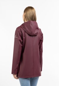 Vandtæt bordeaux jakke med hætte, der har en glat tekstur, lange ærmer og diskret branding på venstre ærme.