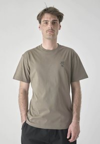 Olive green cotton t-shirt with short sleeves, featuring a small black bird logo on the left chest. Soft texture, classic crew neck design.