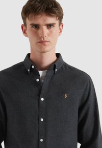 Ciemnoszara koszula zapinana na guziki, wykonana z teksturowanej tkaniny, z małym pomarańczowym haftowanym logo, białymi guzikami i klasycznym kołnierzykiem.