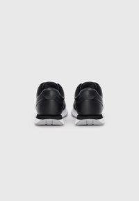 Un paio di sneaker sportive nere con suole bianche, viste da dietro su uno sfondo bianco semplice.