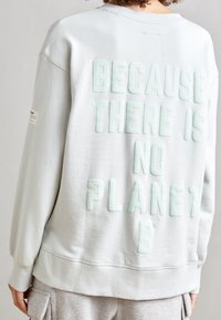 Světle šedá mikina s vystouplým mátově zeleným textem: "PROTOŽE NEEXISTUJE PLANETA B." Měkká bavlněná tkanina s žebrovanými manžetami a spodním lemem.