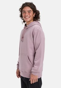 Sudadera con capucha rosa que cuenta con un bolsillo frontal, capucha con cordones, puños acanalados y un logo bordado en el pecho. Textura de tela suave.