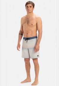 Costume da bagno da uomo grigio con cintura elastica blu. Presenta righe orizzontali, coulisse e logo sul lato sinistro inferiore. Materiale leggero.