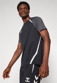 Zwart sport T-shirt met grijze accenten, voorzien van korte mouwen en een ronde halslijn. Witte strepen langs de zijkanten en een logo op de borst.