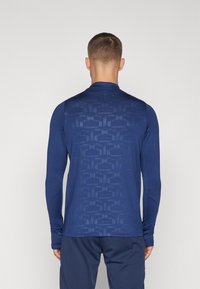 Langarm sportshirt in marineblauw, met een gestructureerd patroon op de achterkant. Gemaakt van lichtgewicht, rekbaar materiaal voor comfort en mobiliteit.