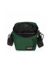 Grön tygaxelväska med ett dragkedjehuvudfack, svart foder, justerbar rem och Eastpak-logotyp på framsidan.