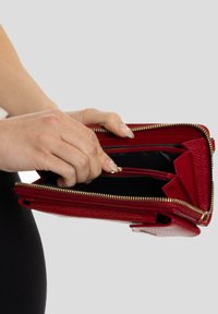 Monedero de cuero rojo con una superficie texturizada, que cuenta con un zipper dorado y múltiples compartimentos. Al abrirlo, se revela un interior negro con un bolsillo con cremallera.