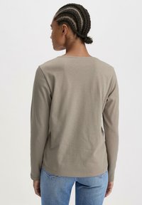 Helles graues Langarmshirt mit lässiger Passform, ausgestattet mit rundem Halsausschnitt und glatter Textur, kombiniert mit blauen Jeans.