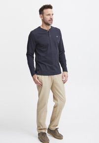 Langermet marineblå henley-skjorte med knappeåpning, kombinert med lyse beige linbukser og brune suedepumps.
