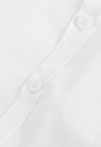 Weißes Hemdenmaterial mit glatter Textur. Verfügt über zwei weiße Knöpfe und eine saubere Leiste. Schlichtes Design ohne sichtbare Muster.