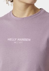 Camiseta lila de algodón suave, con cuello redondo y un logo blanco "HELly HANSEN // 1877" impreso en el pecho.