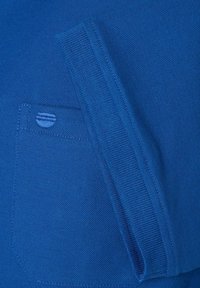 Blauwe geweven stof met een klein zakdetail en ribbelrand. Het materiaal lijkt zacht en het ontwerp is eenvoudig en functioneel.