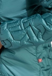 Teal pufferjack met een gewatteerd patroon op de mouwen, gemaakt van glanzende, waterafstotende stof. Heeft Primaloft-label op de zoom.