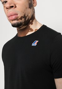 T-shirt nera in cotone con colletto rotondo e un piccolo logo K-Way multicolore sul lato sinistro del petto. Texture liscia e design aderente.
