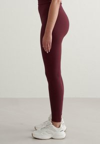 Burgundowe legginsy prążkowane z wysokim pasem, dopasowanym krojem i gładką fakturą, w połączeniu z białymi butami sportowymi.